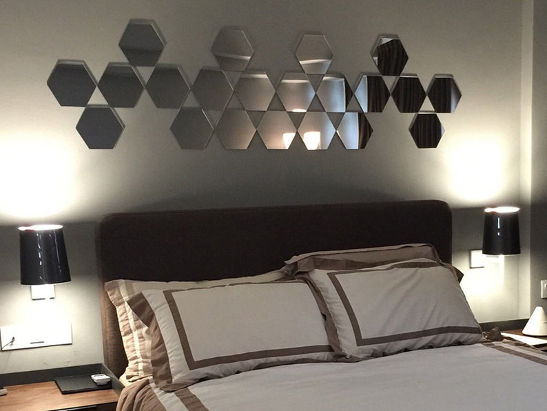 Puede incluir: Un dormitorio con una cama, dos l&aacute;mparas de noche y una pared decorada con un patr&oacute;n geom&eacute;trico de espejos hexagonales.