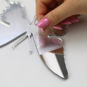 May include: A silver mirrored butterfly wall decoration with a protective film being peeled off. The butterfly has a detailed design and a reflective surface.