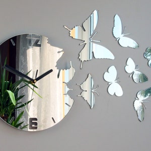 May include: A mirrored clock with a black clock face and hands. The clock is surrounded by mirrored butterflies.