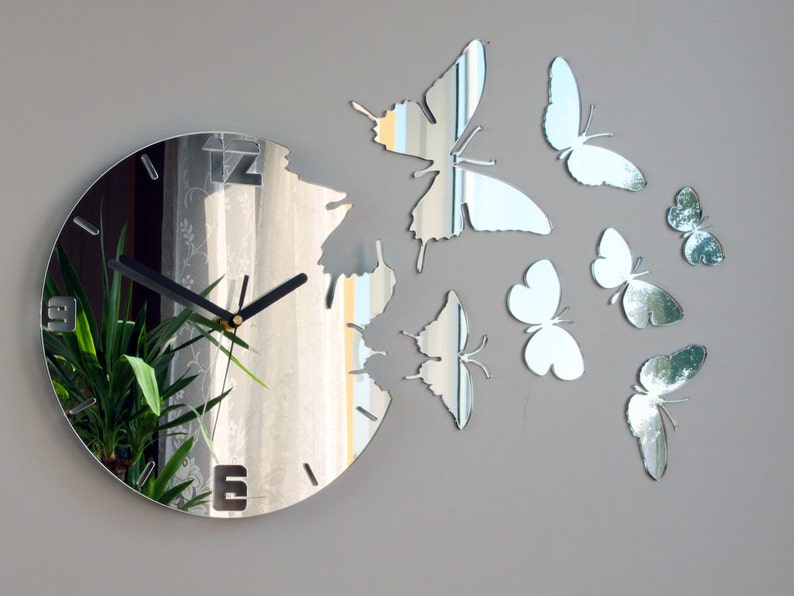 May include: A mirrored clock with a black clock face and hands. The clock is surrounded by mirrored butterflies.