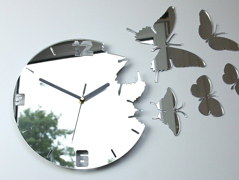 May include: A silver mirrored clock with a unique design featuring a broken edge and butterfly accents. The clock face has Roman numerals and black hands.