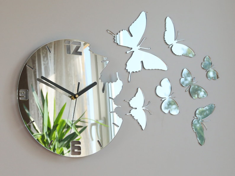 May include: A silver mirrored clock with a butterfly design. The clock face is round and has black hands. The butterflies are cut out of the mirror and are attached to the clock face.