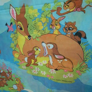 May include: A light blue fabric featuring a colourful print of Bambi characters including a deer, a rabbit, a raccoon, and an owl in a forest setting. The scene includes green foliage, small white and pink flowers, and the text Walt Disney Productions.