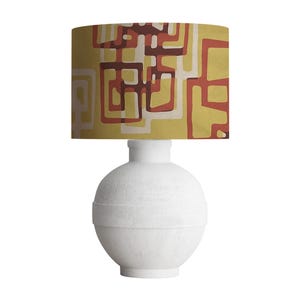 May include: A white ceramic table lamp with a spherical base and a cylindrical neck. The lampshade features a geometric pattern in shades of yellow, red, and brown. The lamp is designed for indoor use and provides ambient lighting.