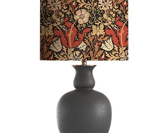 May include: A black ceramic table lamp with a floral patterned lampshade. The lampshade features a repeating pattern of red, orange, yellow, and white flowers on a black background.