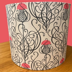 May include: A beige lampshade with a black and pink floral pattern. The pattern features stylized thistles with pink flowers and black swirling vines.