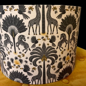 May include: A black and white lampshade with a pattern of giraffes, zebras, palm trees, and toucans on a cream background.