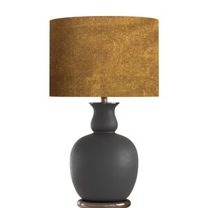 May include: A modern table lamp with a dark gray base and a textured gold lampshade. The lamp has a rounded base and a slender neck, with a metallic accent at the base and the top of the base.