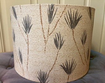May include: Cylindrical lampshade with a cream-colored background and a repeating pattern of dark brown and black stylized plant-like shapes. The lampshade is made of a textured fabric.