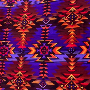 May include: Close-up of a fabric with a geometric pattern in shades of purple, orange, and brown. The design features repeating diamond and arrow shapes, creating a Southwestern or Native American inspired aesthetic. The fabric has a textured appearance.