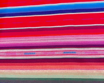 Könnte beinhalten: Ein farbenfroher gestreifter Stoff mit roten, blauen, grünen, rosa und gelben Streifen. Der Stoff ist mit einem strukturierten Muster gewebt.