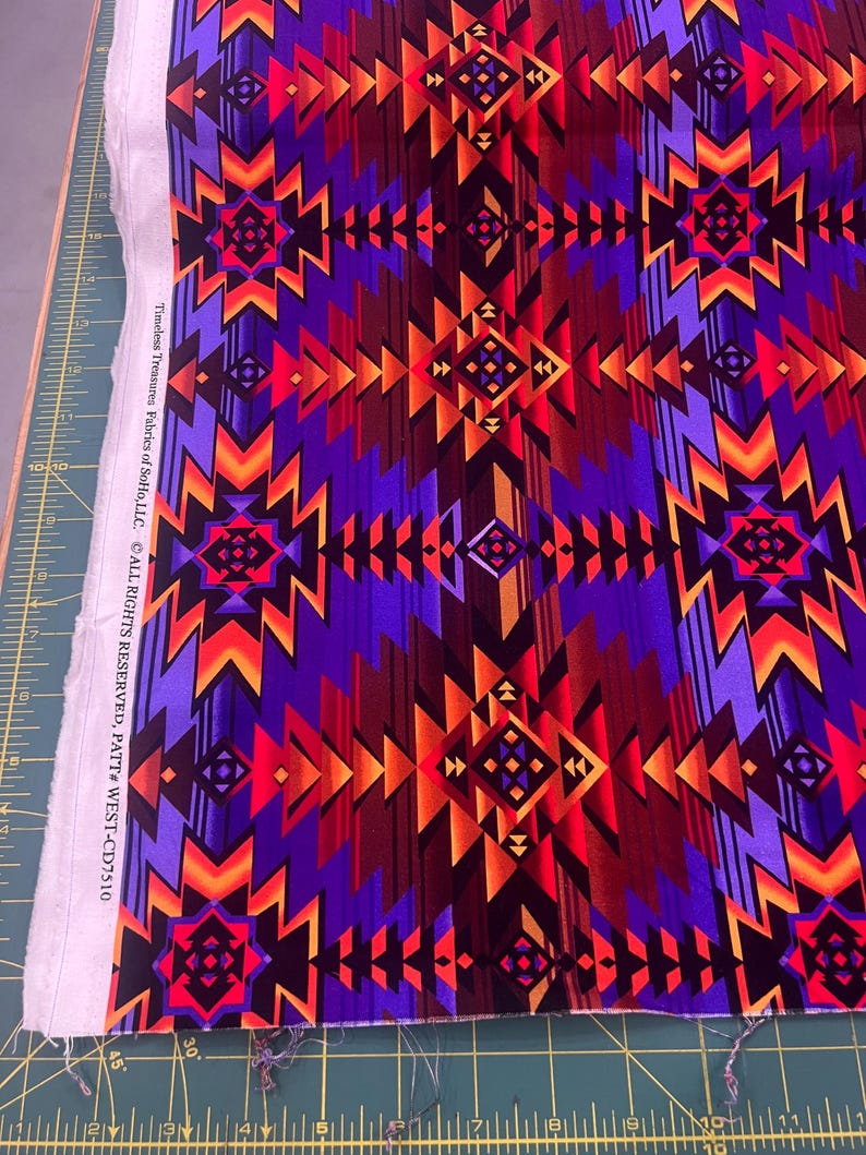 Puede incluir: Una tela vibrante con un patr&oacute;n geom&eacute;trico en tonos de morado, rojo, naranja y marr&oacute;n. El dise&ntilde;o presenta formas angulares repetidas y motivos de diamantes. La tela est&aacute; etiquetada como "Timeless Treasures Fabrics of SoHo, LLC."