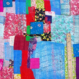 May include: A colorful patchwork quilt with a variety of fabrics and patterns, including floral, paisley, and geometric designs. The quilt is made up of many different squares and rectangles, and the colors are bright and vibrant. A ruler is visible in the bottom right corner of the image.