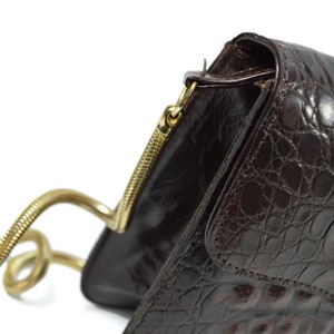 May include: A brown leather handbag with a gold chain strap. The bag has a textured crocodile pattern and a flap closure.