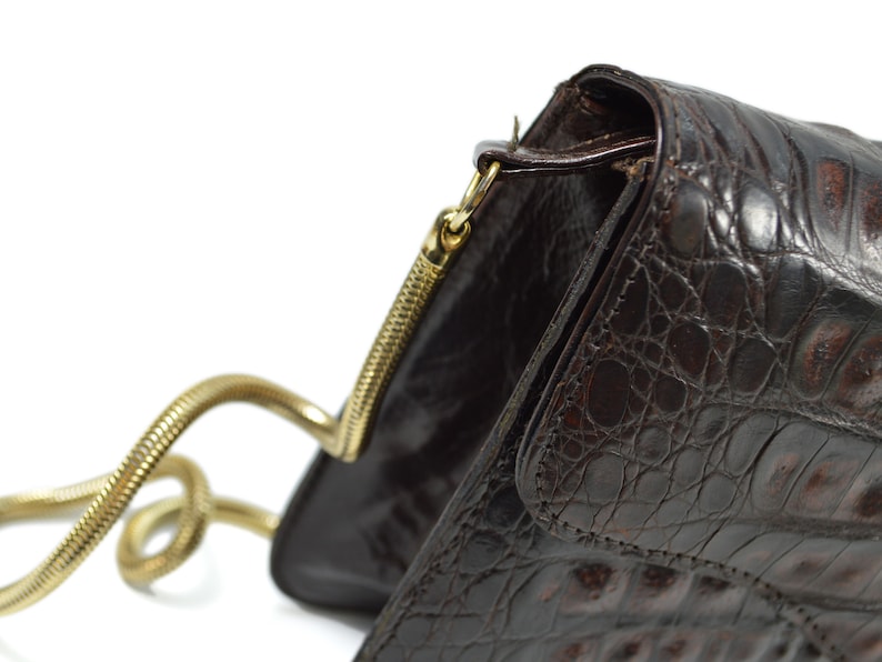 May include: A brown leather handbag with a gold chain strap. The bag has a textured crocodile pattern and a flap closure.