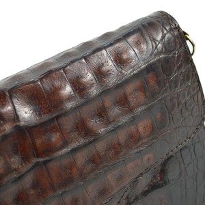 May include: A brown leather handbag with a crocodile-embossed pattern. The bag has a flap closure and a shoulder strap.