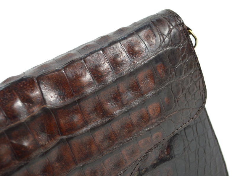 May include: A brown leather handbag with a crocodile-embossed pattern. The bag has a flap closure and a shoulder strap.