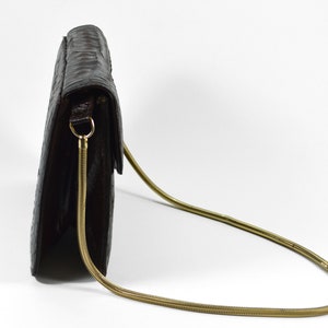 May include: A brown leather clutch bag with a gold chain strap. The bag has a flap closure and a textured surface.