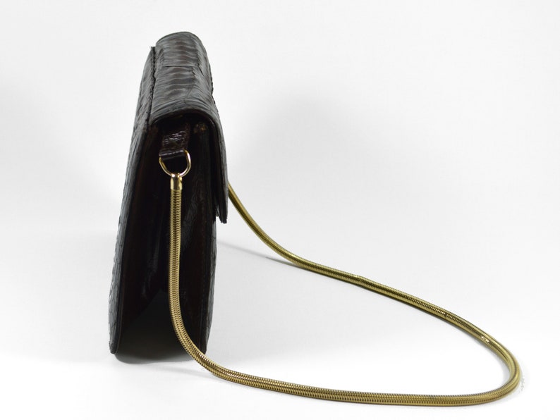 May include: A brown leather clutch bag with a gold chain strap. The bag has a flap closure and a textured surface.