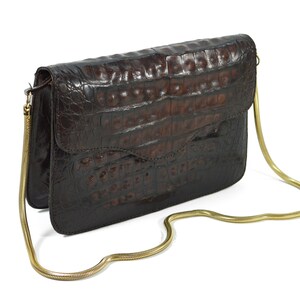May include: A brown crocodile-embossed leather clutch bag with a gold chain strap.