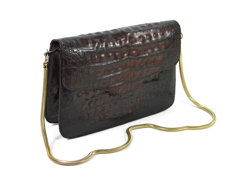 May include: A brown crocodile-embossed leather clutch bag with a gold chain strap.