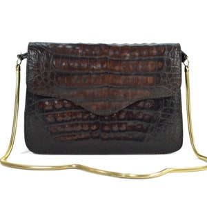 May include: A brown crocodile leather clutch bag with a gold chain strap.