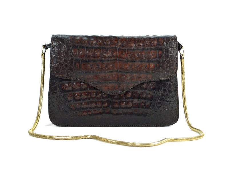 May include: A brown crocodile leather clutch bag with a gold chain strap.