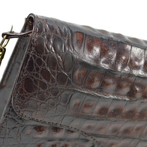 May include: A brown crocodile leather handbag with a gold chain strap.