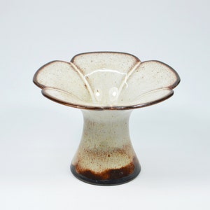 Pode incluir: Um vaso de cerâmica branco com um esmalte castanho. O vaso tem uma abertura larga em forma de flor e uma base estreita.