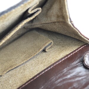 May include: The inside of a brown leather wallet with a suede lining. The wallet has multiple pockets and a snap closure.
