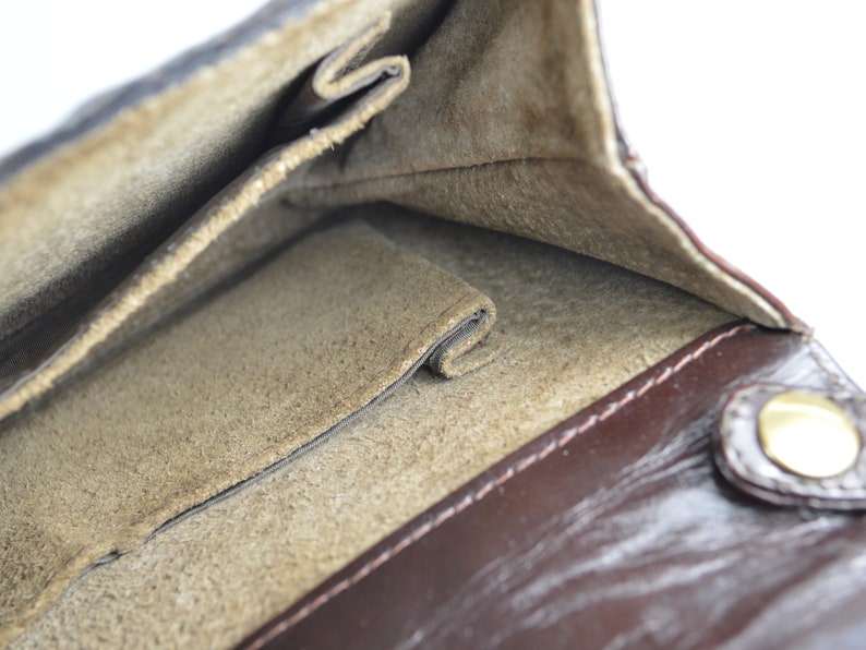 May include: The inside of a brown leather wallet with a suede lining. The wallet has multiple pockets and a snap closure.