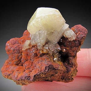 May include: A cluster of translucent, pale yellow baryte crystals on a matrix of reddish-brown iron oxide. The crystals are sharp and well-formed, with a glassy lustre.