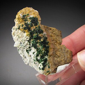 May include: A small rock specimen with a cluster of green crystals on a white and brown matrix.