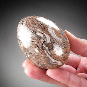 May include: A smooth, oval-shaped stone with a swirling pattern of brown, white, and black. The stone is polished and has a glossy finish.