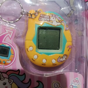 May include: A yellow and blue plastic keychain with a digital screen and buttons. The keychain features a unicorn and the text "Pet Game Console".