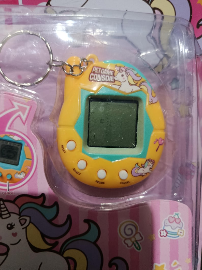May include: A yellow and blue plastic keychain with a digital screen and buttons. The keychain features a unicorn and the text "Pet Game Console".