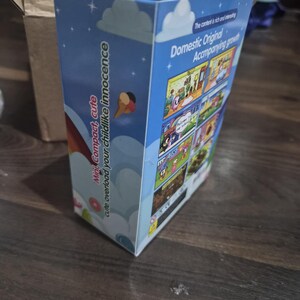 May include: A rectangular cardboard product box with a light blue background featuring white clouds and stars. The side panel displays the text "Mini Compact, cute overload your childlike innocence" and the back panel shows various cartoon scenes.