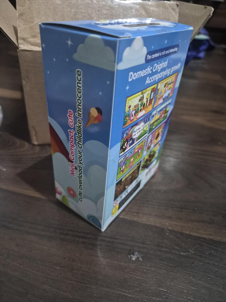 May include: A rectangular cardboard product box with a light blue background featuring white clouds and stars. The side panel displays the text "Mini Compact, cute overload your childlike innocence" and the back panel shows various cartoon scenes.