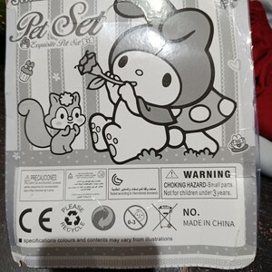 May include: A black and white illustration of a cartoon character holding a flower. The character is wearing a hooded dress with polka dots. The image also includes a squirrel and the text "Pet Set Exquisite Pet Set". The packaging includes a warning label that reads "CHOKING HAZARD - Small parts. Not for children under 3 years."