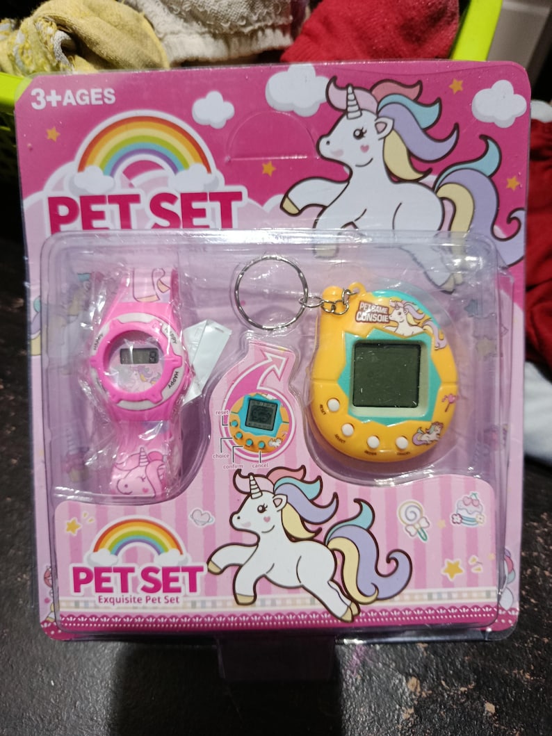 May include: A pink and yellow packaging with a unicorn design. The packaging contains a pink watch with a unicorn design, a yellow digital pet toy with a unicorn design, and a keychain with a unicorn design. The packaging says "Pet Set Exquisite Pet Set" and "3+ Ages".