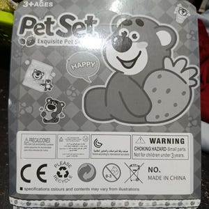 May include: A gray cardboard box with a cartoon bear holding a strawberry. The box has the words "Pet Set" and "Happy" on it. The box also has a warning label that says "Choking Hazard - Small parts. Not for children under 3 years."