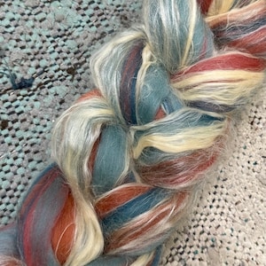 May include: A braid of yarn in shades of cream, rust, and teal. The yarn is soft and fluffy, and it would be perfect for knitting or crocheting.