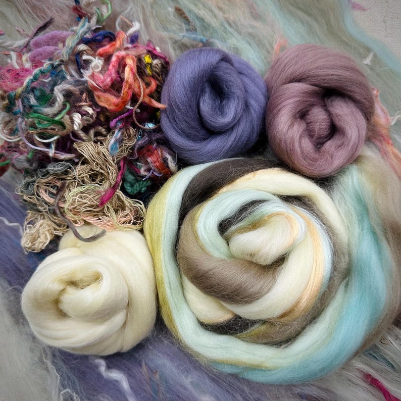 May include: A collection of colorful wool roving in shades of purple, brown, white, and blue. The wool is arranged in a circular pattern, with the different colors overlapping.