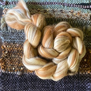 May include: A braided bundle of brown and white wool roving. The roving is arranged in a circular shape, with the ends of the braid tucked into the center.