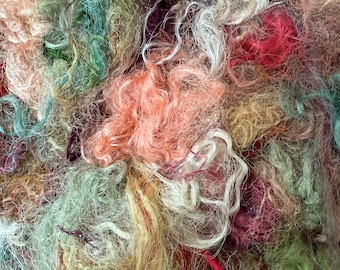 May include: A close-up of a pile of colorful fiber strands. The fibers are in shades of pink, peach, green, yellow, and white. The texture appears soft and fluffy, with some strands appearing more coarse.