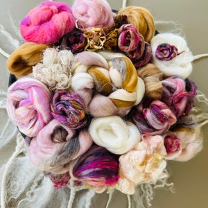 May include: A collection of colorful yarn and fiber rovings in shades of pink, purple, brown, and white. The fibers are arranged in a circular pattern, creating a visually appealing and textured display.