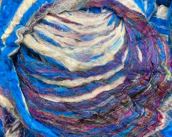 May include: A close-up of a bundle of colorful yarn in shades of blue, white, and purple. The yarn is arranged in a spiral pattern, creating a textured and abstract design.