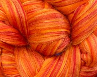 May include: Close-up of a vibrant bundle of orange and red fiber. The fiber is tightly packed, with visible strands of varying shades creating a striped effect. The texture appears soft and fluffy, ideal for crafting projects.