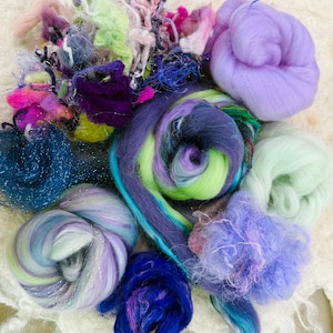 May include: A collection of colorful fiber art materials, including various shades of purple, blue, green, and pink. The assortment features fluffy wool roving, sparkly threads, and textured fibers, ideal for crafting and textile projects.