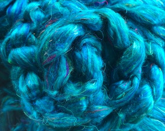 May include: A close-up of a teal blue fiber with a variety of colors woven throughout. The fiber is soft and fluffy, and it appears to be made of natural materials.